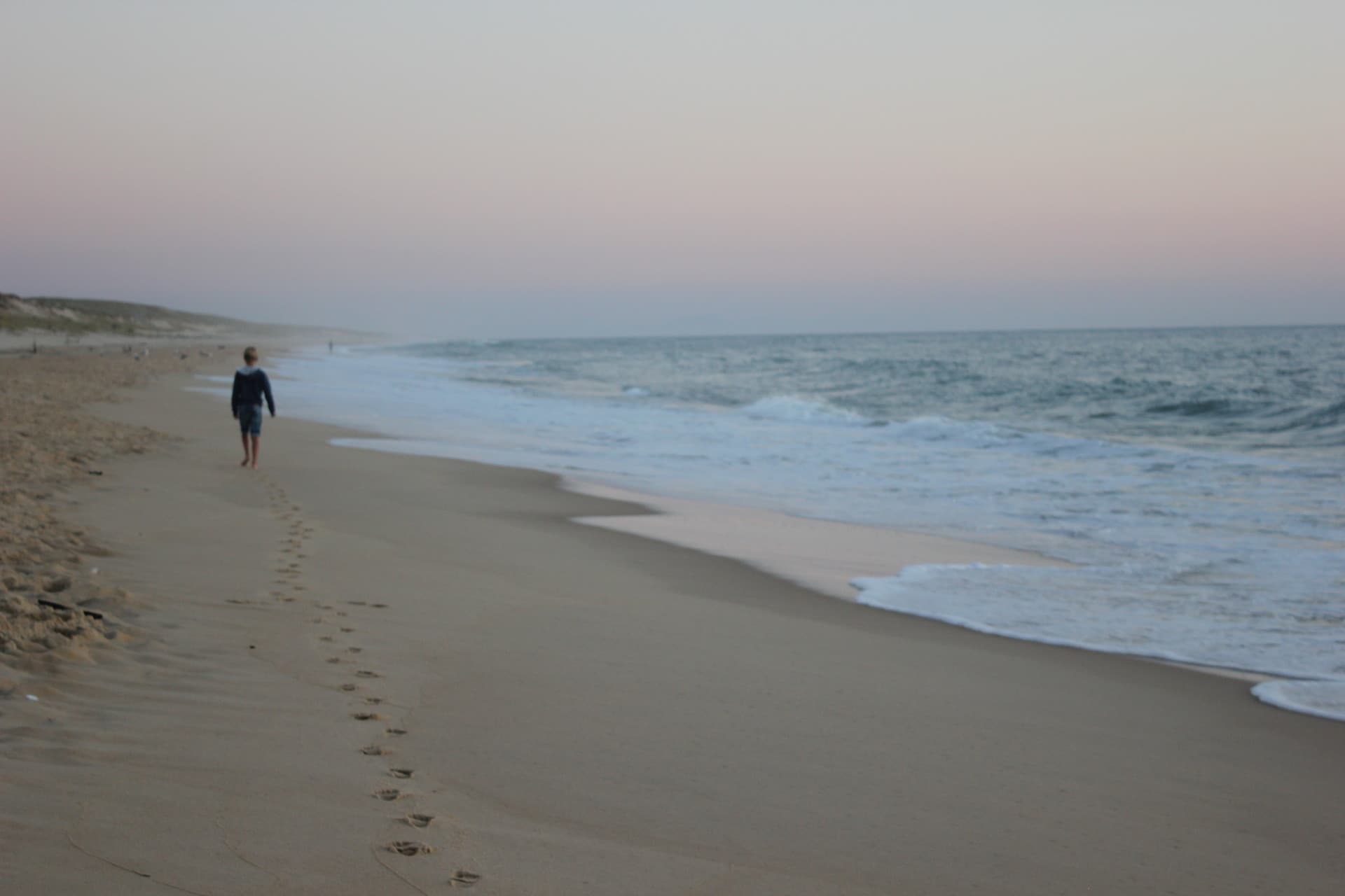 Een kind loopt langs de zee bij zacht ochtendlicht, met voetstappen in het zand