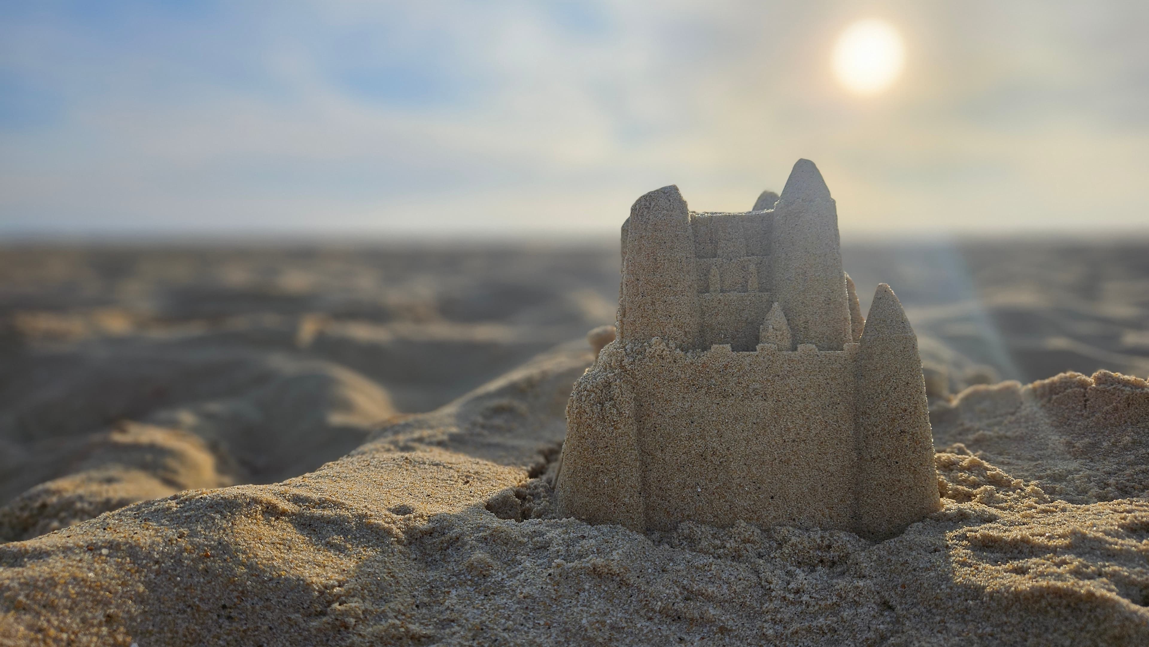 Zandkasteel op het strand, met de zon en een warme zonnestraal langs de torens