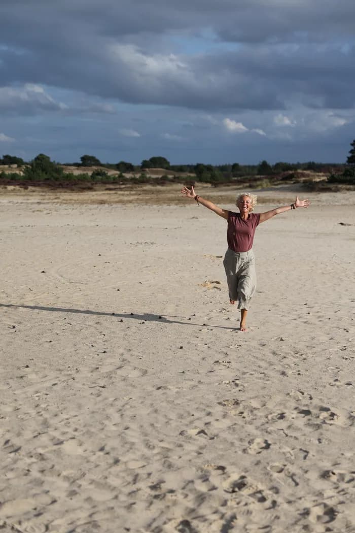 Simone loopt met open armen door het duinlandschap