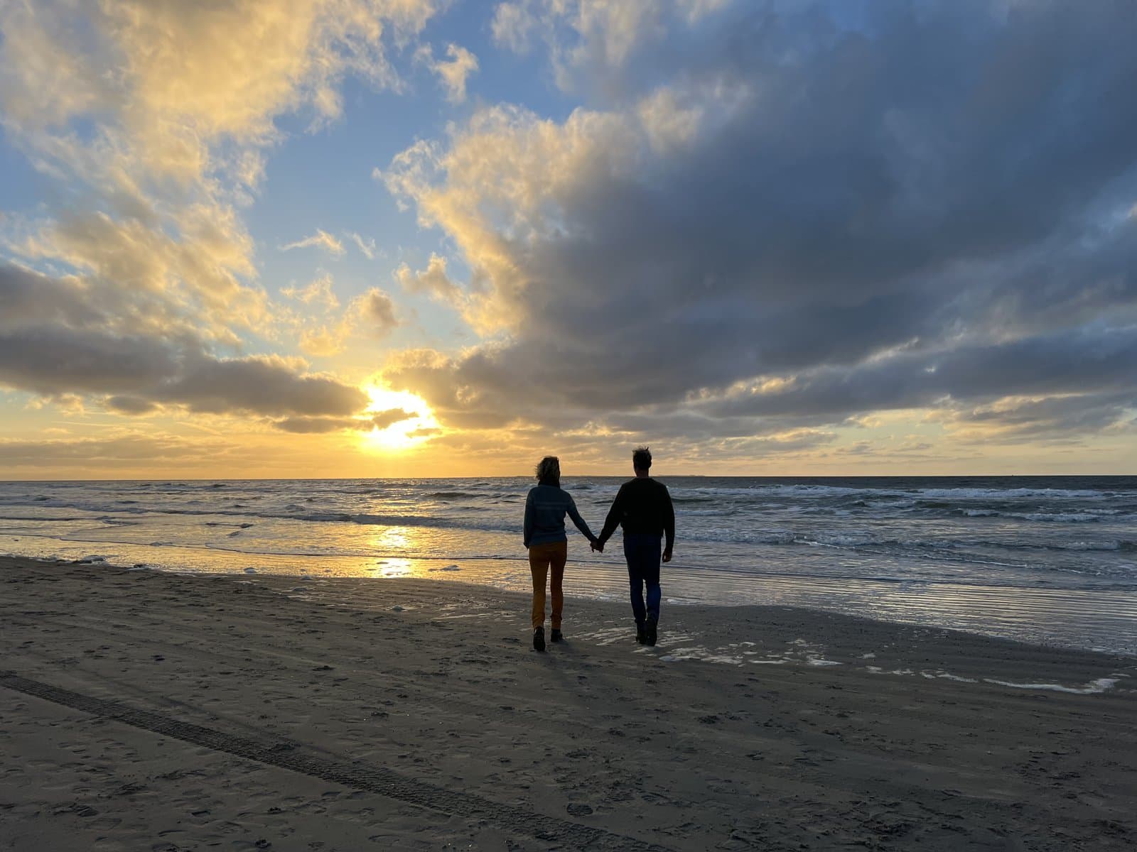 Twee mensen lopen hand in hand op het strand richting de zonsondergang - samen erbij horen